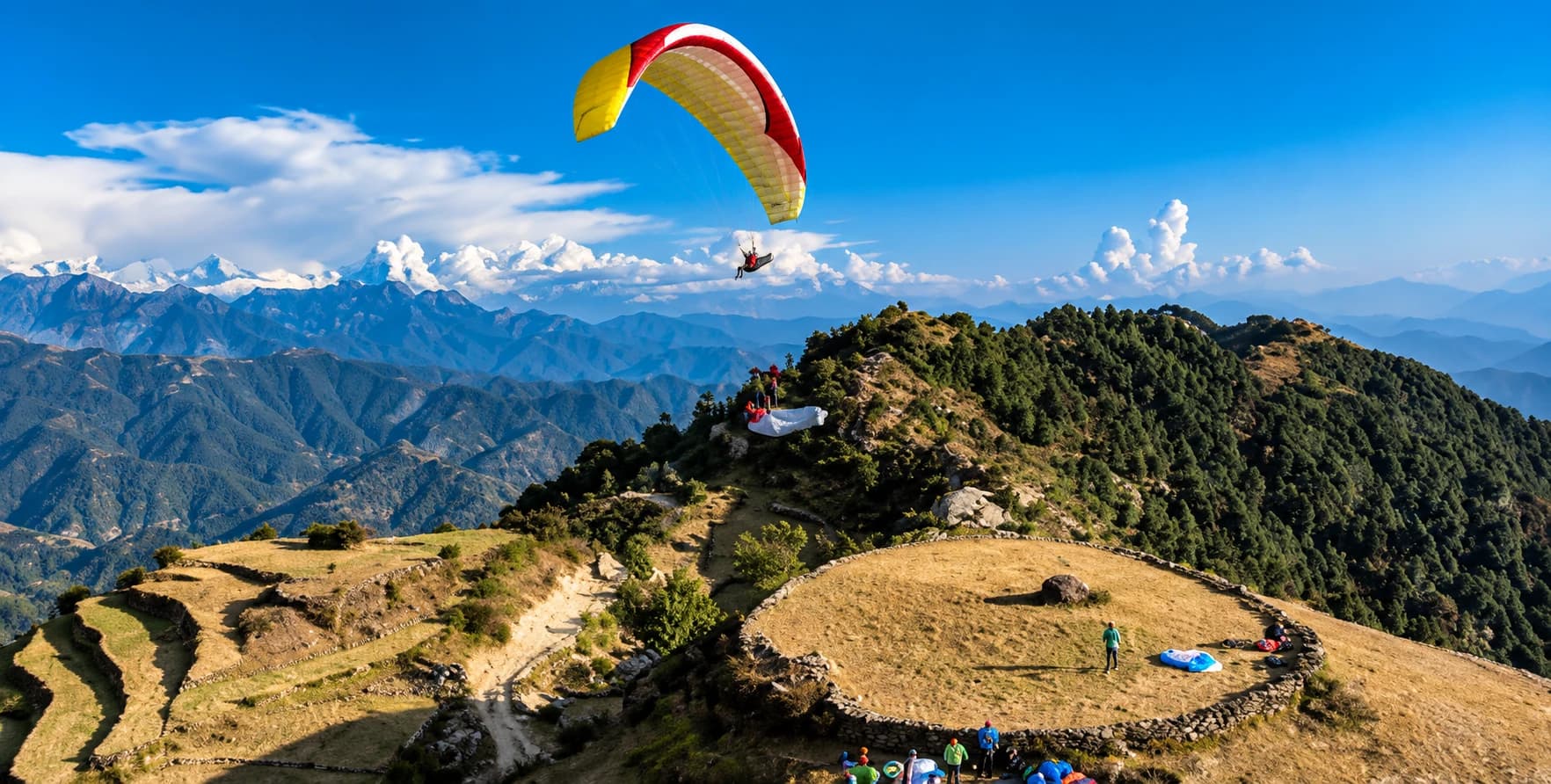 A paraglider soaring above the Bir Billing launch site with Himalayan peaks in the distance