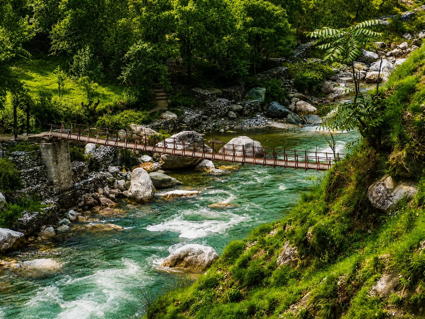 A footbridge over the flowing Tirthan river